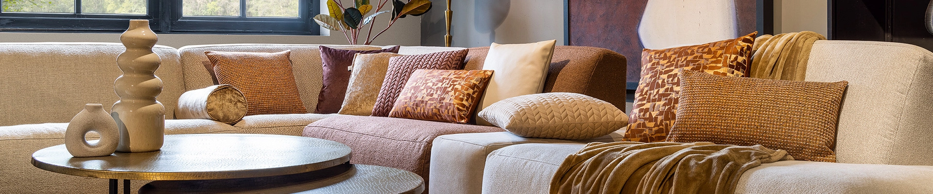dutch-decor-sierkussens-en-plaids-in-aardetitnten Een comfortabele bank met kleurrijke sierkussens en een fleece plaid, perfect voor een gezellige woonkamer.