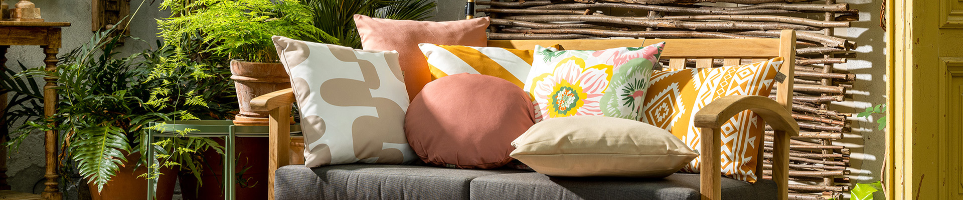 Een comfortabele tuinbankje met kleurrijke kussens  van Dutch Decor erop. Perfect om in te ontspannen en tot rust te komen.